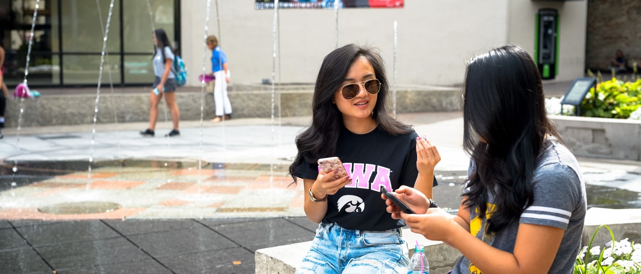 Two people sitting on a bench near the fountains at the Ped Mall