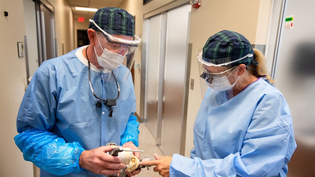 Two people in surgical attire and face shields looking at a model of the human mouth